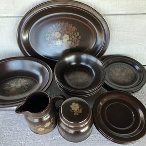 May include: A set of brown stoneware dinnerware with a floral design. The set includes a large oval platter, a large bowl, a set of smaller bowls, a creamer, a sugar bowl, and a set of saucers.