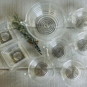 May include: Set of seven clear glass bowls with a concentric circle pattern. The bowls are various sizes and shapes, including a large bowl with a handle.