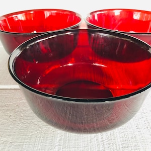 May include: Three red glass bowls, each with a slightly different shade of red. The bowls are stacked on top of each other, with the largest bowl on the bottom and the smallest bowl on top.