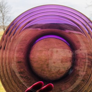 May include: A purple glass plate with a rippled design. The plate is clear and has a slight iridescent sheen.