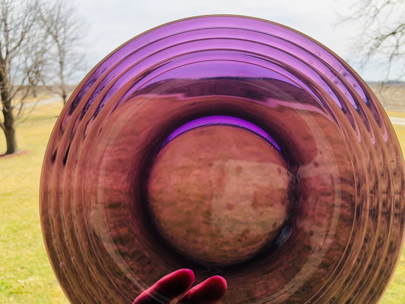 May include: A purple glass plate with a rippled design. The plate is clear and has a slight iridescent sheen.