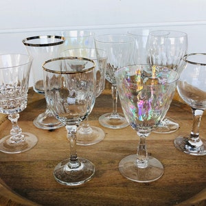 May include: A set of eight clear glass wine glasses with gold rims. The glasses are arranged on a wooden tray.