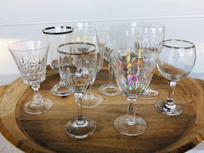 May include: A set of eight clear glass wine glasses with gold rims. The glasses are arranged on a wooden tray.