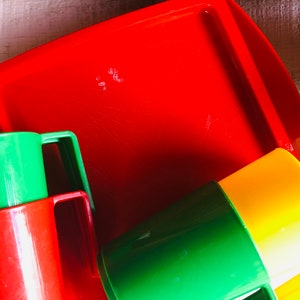Puede incluir: Una bandeja de pl&aacute;stico roja con tres vasos de pl&aacute;stico de colores. Los vasos son verdes, rojos y amarillos. Los vasos tienen asas.