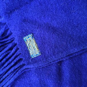 K&ouml;nnte beinhalten: Ein k&ouml;nigsblauer Pendleton Wollschal mit Fransen an den Enden. Der Schal hat ein blaues Etikett mit dem Pendleton-Logo und dem Aufdruck "WARRANTED TO BE A PENDLETON WOOL PRODUCT".