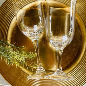 May include: Two clear glass wine glasses with gold rims on a gold charger plate.