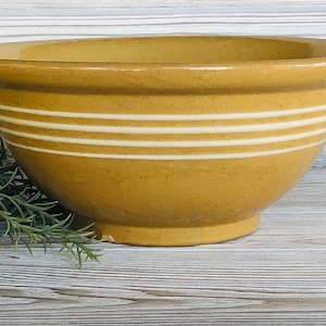 May include: A yellow ceramic mixing bowl with white stripes. The bowl is glazed and has a smooth finish.