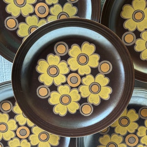 May include: Set of five brown ceramic dinner plates with a floral pattern in yellow and orange. The plates have a raised rim and a slightly textured surface.