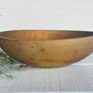 May include: A large, oval-shaped wooden bowl with a natural, aged finish. The bowl has a smooth interior and exterior, with visible wood grain and slight imperfections. The color is a warm, medium brown, suggesting it's been well-used.