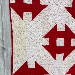 Peut inclure: Gros plan sur une courtepointe rouge et blanche avec un motif de maison r&eacute;p&eacute;titif. Les maisons rouges ont un carr&eacute; blanc au centre, sur un fond blanc. Le fil rouge cr&eacute;e un motif d&eacute;coratif et tourbillonnant entre les maisons.