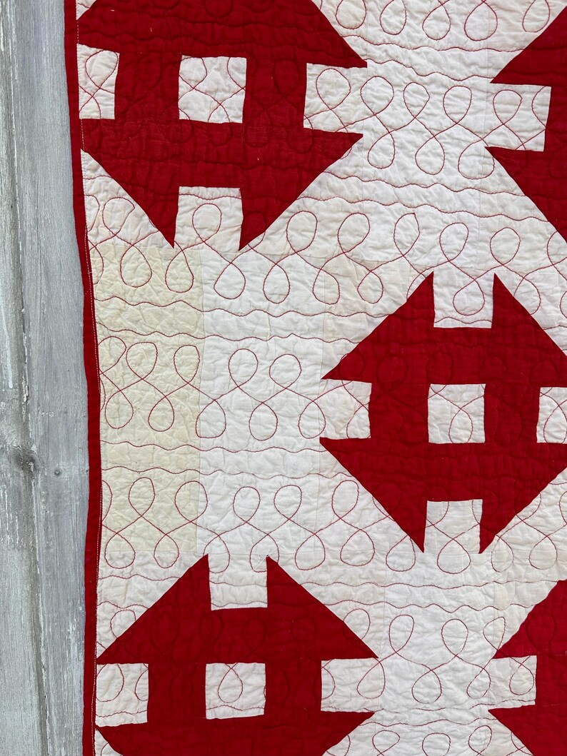 Peut inclure: Gros plan sur une courtepointe rouge et blanche avec un motif de maison r&eacute;p&eacute;titif. Les maisons rouges ont un carr&eacute; blanc au centre, sur un fond blanc. Le fil rouge cr&eacute;e un motif d&eacute;coratif et tourbillonnant entre les maisons.