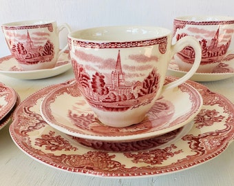 May include: A set of four vintage teacups and saucers with a pink floral pattern. The cups and saucers feature a delicate floral design with a church in the background.
