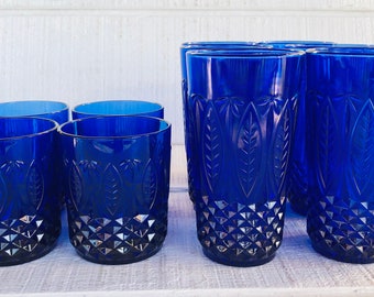 May include: A collection of cobalt blue glass tumblers in two different heights. Each glass features a textured diamond pattern at the base and a vertical leaf motif embossed around the upper body, creating a uniform set of drinking vessels.