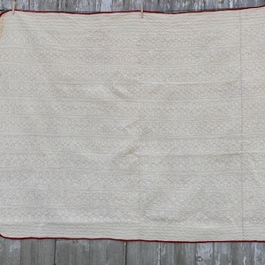 Peut inclure: Une courtepointe rectangulaire cr&egrave;me avec une bordure rouge, suspendue &agrave; une corde &agrave; linge. La courtepointe pr&eacute;sente un motif r&eacute;p&eacute;titif de boucles interconnect&eacute;es de couleur cr&egrave;me plus claire, cr&eacute;ant un effet textur&eacute;. Le design g&eacute;n&eacute;ral est simple et classique.