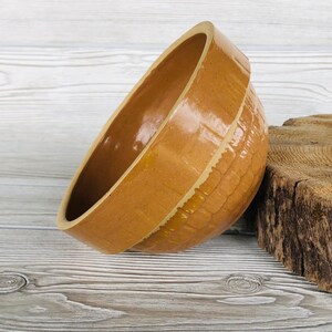 May include: A large, brown ceramic mixing bowl with a textured surface. The bowl is glazed with a light brown color and has a white rim.