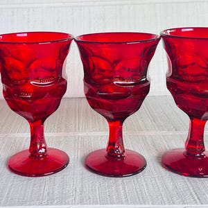 May include: Set of five red glass wine goblets with a cut glass design.