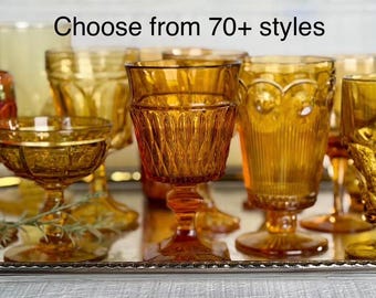 May include: A collection of amber and orange colored glass goblets and drinking glasses with various embossed patterns and textures. The text "Choose from 70+ styles" is displayed at the top of the image. The glassware is arranged on a silver tray.