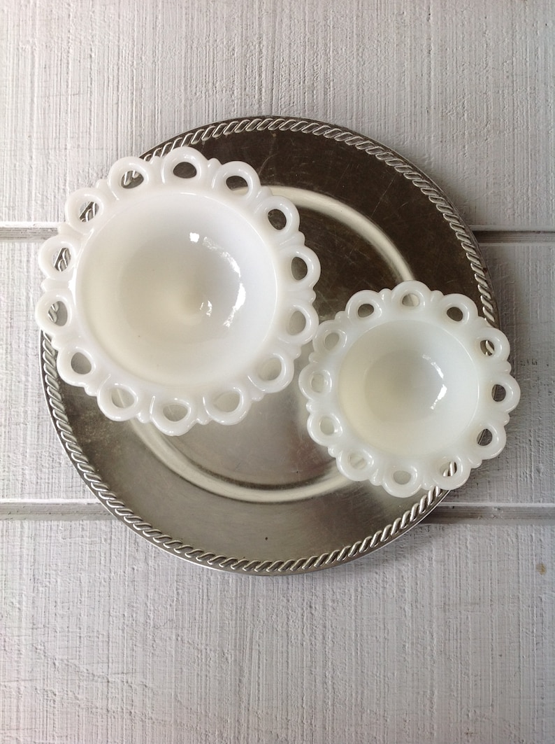 May include: Two white milk glass bowls with scalloped edges sit on a silver charger. The bowls are different sizes and have a vintage look.