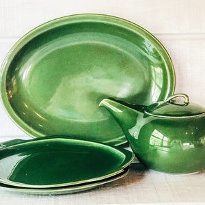 May include: A set of green ceramic dishes, including a large oval serving platter, two smaller oval plates, and a teapot. The dishes have a glossy finish and a deep green color.