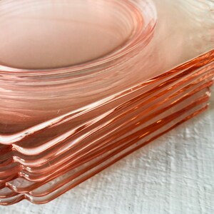 May include: A stack of pink glass plates with scalloped edges. The plates are stacked on top of each other, with the top plate being the most visible.