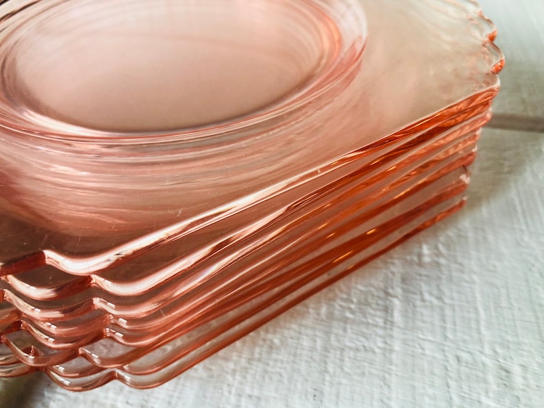 May include: A stack of pink glass plates with scalloped edges. The plates are stacked on top of each other, with the top plate being the most visible.