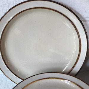 Może przedstawiać: Zestaw białych ceramicznych talerzy obiadowych z brązową obw&oacute;dką. Talerze mają kropkowaną glazurę i prosty wz&oacute;r.