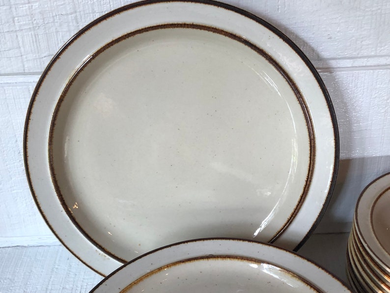 Może przedstawiać: Zestaw białych ceramicznych talerzy obiadowych z brązową obw&oacute;dką. Talerze mają kropkowaną glazurę i prosty wz&oacute;r.