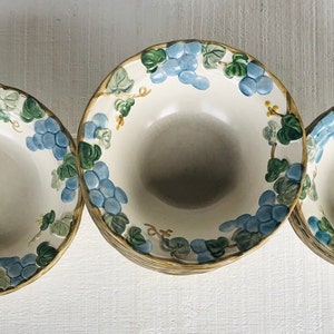 May include: Three white ceramic bowls with blue and green grape designs. The bowls are nested together, with the largest bowl in the back and the smallest bowl in the front.