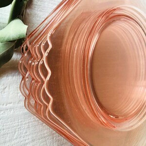 May include: A stack of pink glass dessert plates with scalloped edges. The plates are stacked on a white surface.