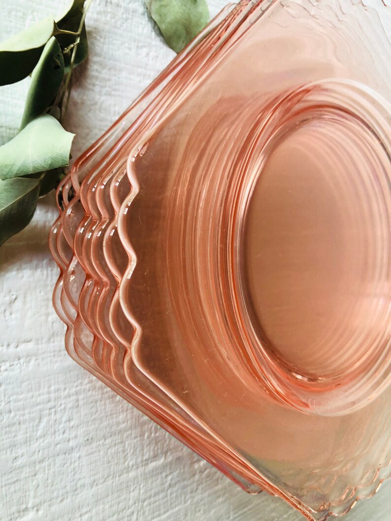 May include: A stack of pink glass dessert plates with scalloped edges. The plates are stacked on a white surface.