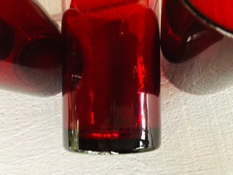 May include: Close-up of three ruby red glass objects. The objects have a glossy finish and are arranged closely together. The lighting creates highlights and shadows, emphasizing the shapes and the rich color of the glass.