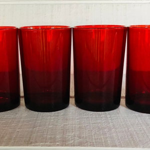 May include: Four red drinking glasses. The glasses are cylindrical with a dark red base that fades to a lighter red at the top. The glasses are made of glass and are empty.