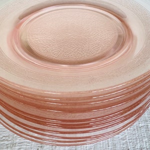 May include: A stack of pink glass dinner plates with a delicate floral pattern. The plates are translucent and have a slightly frosted finish.