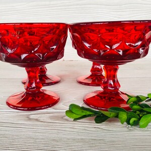 May include: Four red glass dessert dishes with a diamond pattern. The dishes are on a white wooden surface.