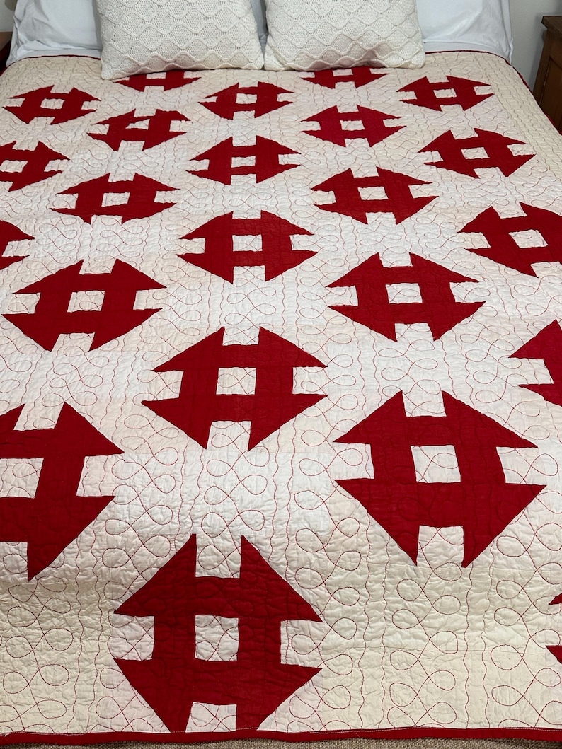 Peut inclure: Une courtepointe faite &agrave; la main avec un motif r&eacute;p&eacute;titif de formes g&eacute;om&eacute;triques rouges sur un fond blanc. La courtepointe est matelass&eacute;e avec du fil rouge, cr&eacute;ant une surface textur&eacute;e. Deux oreillers d&eacute;coratifs blancs sont visibles en haut du lit.