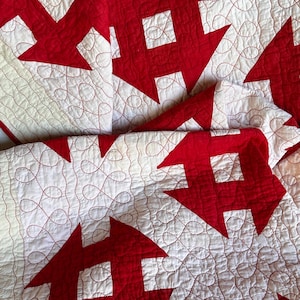 Peut inclure: Gros plan sur une courtepointe faite &agrave; la main avec un motif r&eacute;p&eacute;titif de formes g&eacute;om&eacute;triques rouges sur un fond blanc. La courtepointe est cousue avec du fil rouge, cr&eacute;ant une surface textur&eacute;e. Le design est de style classique et traditionnel.