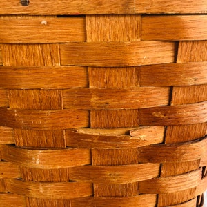 Puede incluir: Primer plano de una cesta de mimbre de madera de color marr&oacute;n natural. La cesta est&aacute; hecha de finas tiras de madera que se entrelazan para crear un recipiente resistente y duradero.