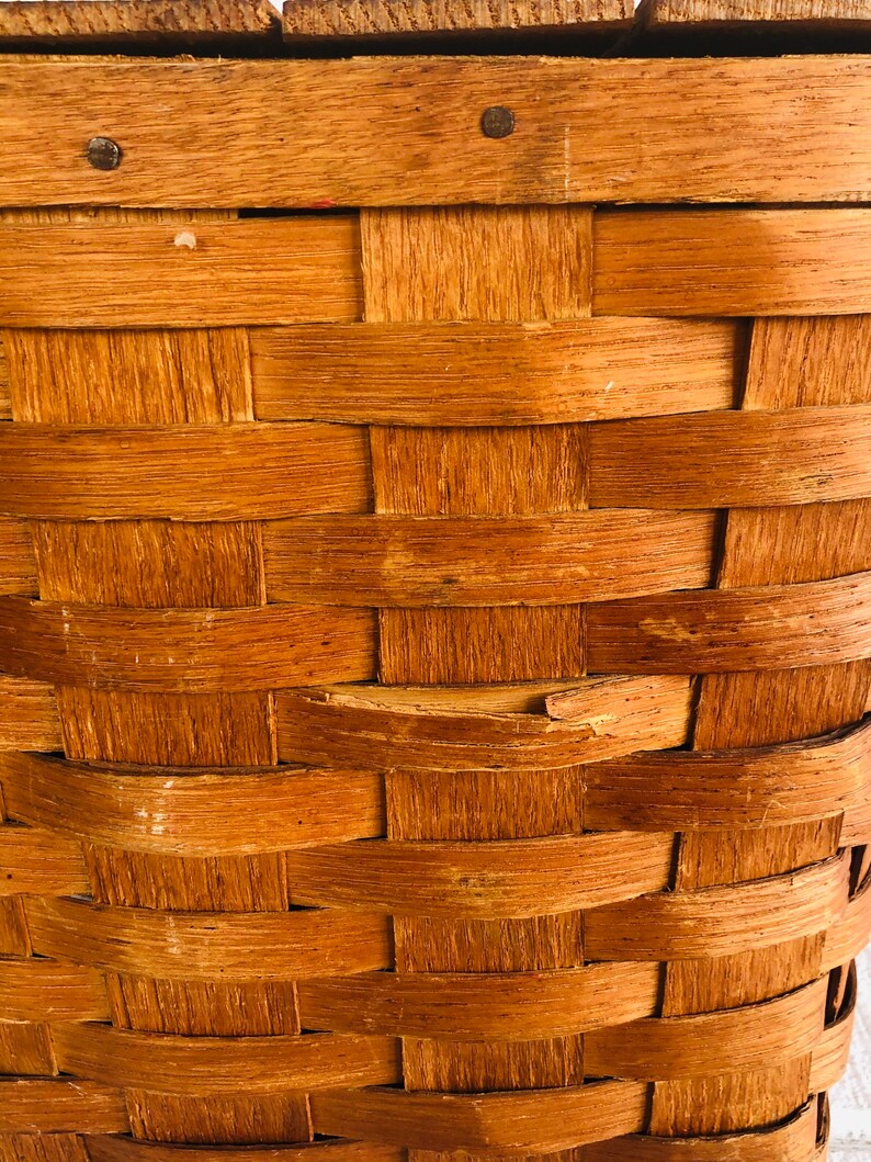 Puede incluir: Primer plano de una cesta de mimbre de madera de color marr&oacute;n natural. La cesta est&aacute; hecha de finas tiras de madera que se entrelazan para crear un recipiente resistente y duradero.
