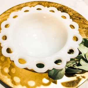May include: A white milk glass bowl with a scalloped edge. The bowl is sitting on a gold-colored surface.