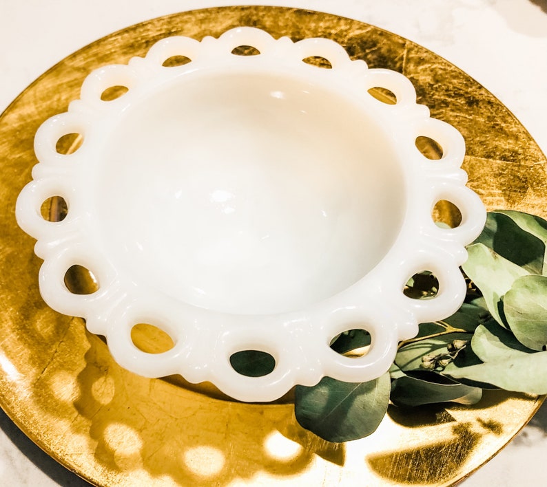 May include: A white milk glass bowl with a scalloped edge. The bowl is sitting on a gold-colored surface.