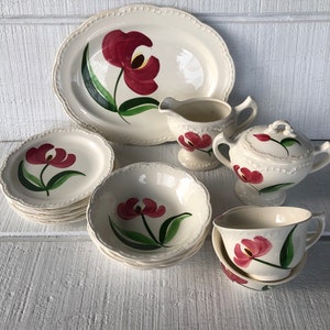 May include: A set of vintage white ceramic dinnerware with a red tulip floral design. The set includes a large platter, a creamer, a sugar bowl, a teacup and saucer, and a set of bowls.