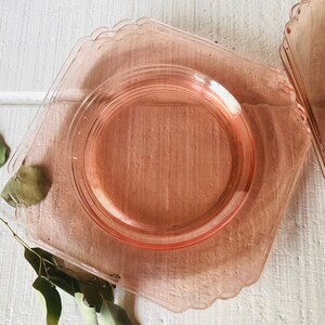 May include: A set of four pink glass dessert plates with scalloped edges. The plates are stacked on top of each other.