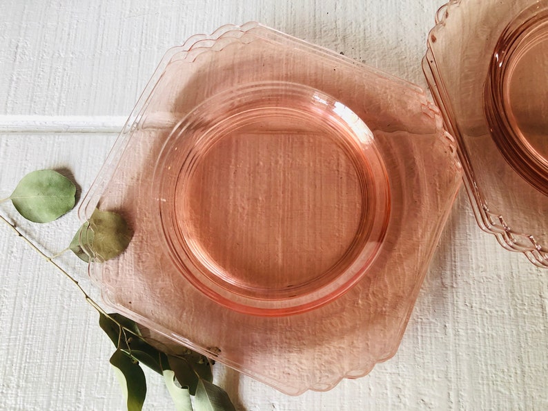 May include: A set of four pink glass dessert plates with scalloped edges. The plates are stacked on top of each other.