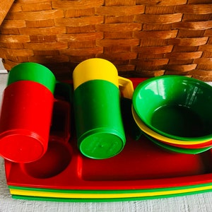 Puede incluir: Un juego de vajilla de picnic de pl&aacute;stico rojo, verde y amarillo. El juego incluye dos tazas, tres cuencos y una bandeja. La bandeja est&aacute; apilada con una capa verde, amarilla y roja.
