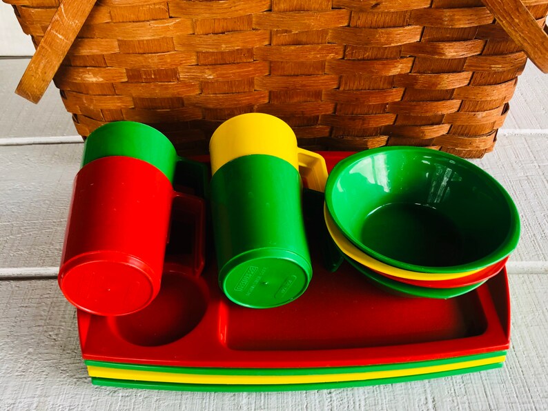 Puede incluir: Un juego de vajilla de picnic de pl&aacute;stico rojo, verde y amarillo. El juego incluye dos tazas, tres cuencos y una bandeja. La bandeja est&aacute; apilada con una capa verde, amarilla y roja.