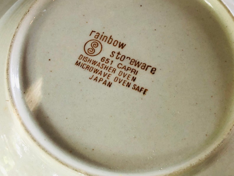 Może przedstawiać: Zbliżenie na sp&oacute;d białego ceramicznego talerza z brązowym tekstem, kt&oacute;ry brzmi "rainbow stoneware 651 CAPRI DISHWASHER OVEN MICROWAVE OVEN SAFE JAPAN".