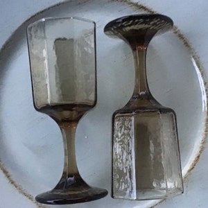 May include: Two clear glass wine glasses with a brown tint and a textured surface. The glasses have a hexagonal base and a stem.
