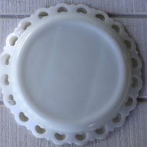 May include: White milk glass plate with a scalloped edge and a delicate lace design. The plate is perfect for serving desserts or snacks.