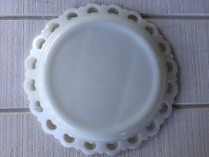 May include: White milk glass plate with a scalloped edge and a delicate lace design. The plate is perfect for serving desserts or snacks.