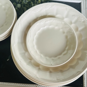 May include: A set of white ceramic plates with a raised wheat design. The plates are nested together, with a smaller bowl in the center.